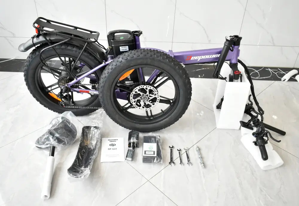 Partially disassembled purple electric bicycle with fat tires and various parts laid out on the floor.